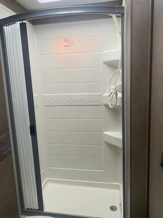 Inside this clean RV rental shower: a compact white stall with textured walls, a handheld shower, and shelves.. Thor Motor Coach Chateau 2020