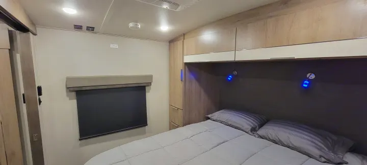 Inside an RV rental: a compact bedroom with bed, overhead cabinets, window, and blue accent lights.. Grand Design 2800BH 2021