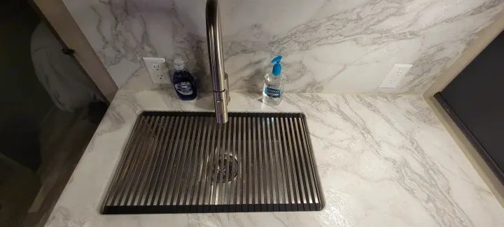 Clean RV rental kitchen with sink, modern faucet, dish soap, sanitizer, and roll-up drying rack on a marble counter.. Grand Design 2800BH 2021