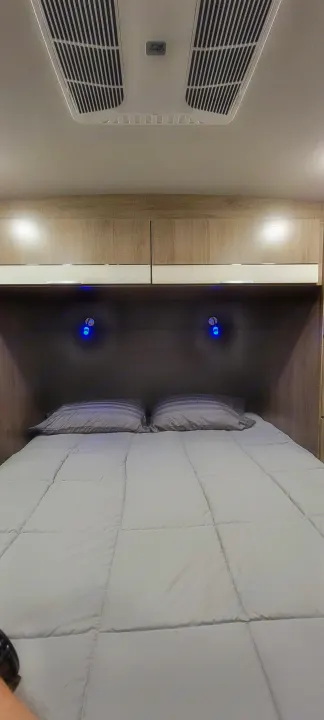 Cozy RV rental bedroom with a neatly made bed, overhead AC unit, and illuminated storage beside the bed.. Grand Design 2800BH 2021