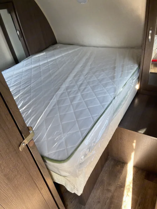 RV rental bedroom with a new, plastic-wrapped mattress, featuring wood cabinetry and a step-down floor.. Forest River Cruise Lite 2019