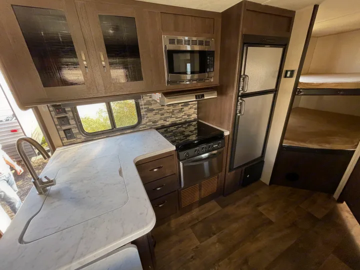 Experience a modern RV rental kitchen featuring a sink, stove, microwave, fridge, and cozy bunk beds for your travels.. Forest River Cruise Lite 2019
