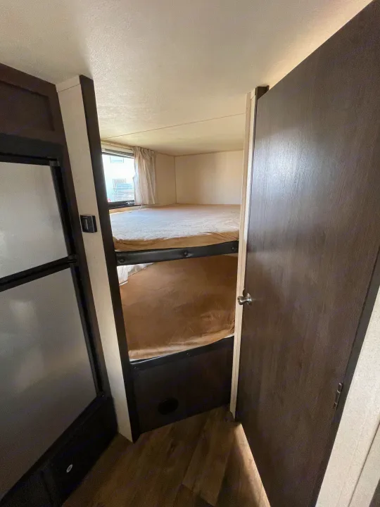 A view of the bunk beds inside an RV rental, featuring light bedding and a window, ideal for extra sleeping.. Forest River Cruise Lite 2019
