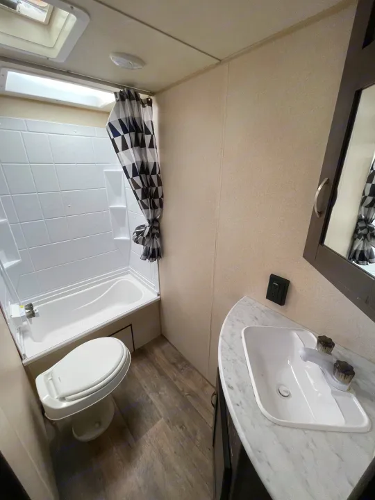 Compact RV rental bathroom with a tub/shower, toilet, sink, and mirror. Perfect for comfortable travel adventures.. Forest River Cruise Lite 2019
