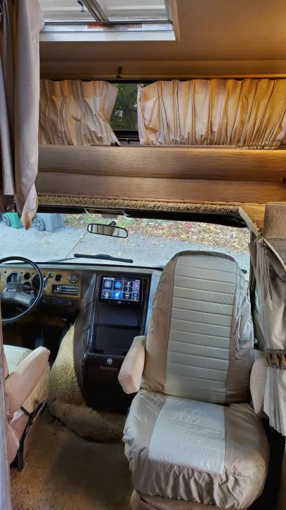 RV rental interior: The driver's cockpit features an updated screen, with a cozy cab-over bunk above.. Lazy Daze 22 1987