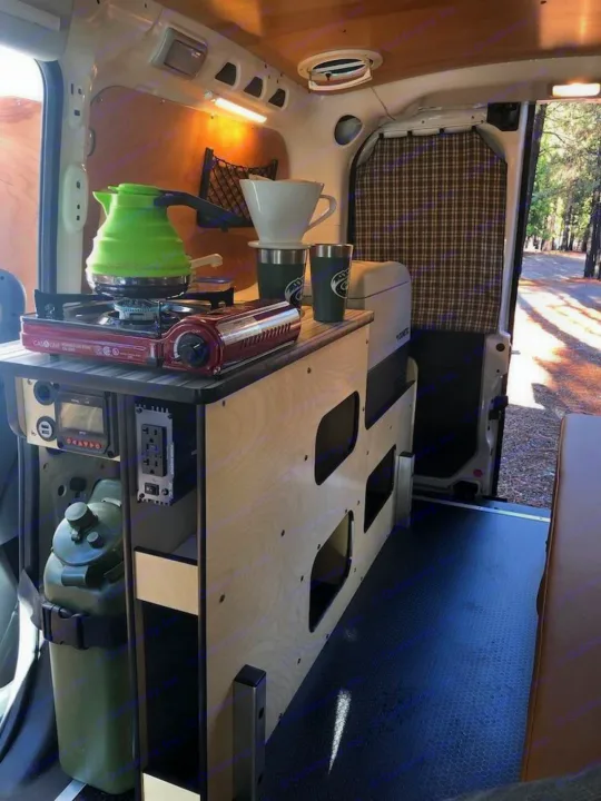 Inside an rv rental: a cozy camper van kitchen with portable stove, coffee gear, and built-in storage, perfect for nature trips.. Cascade Campers Ram Promaster City 2018