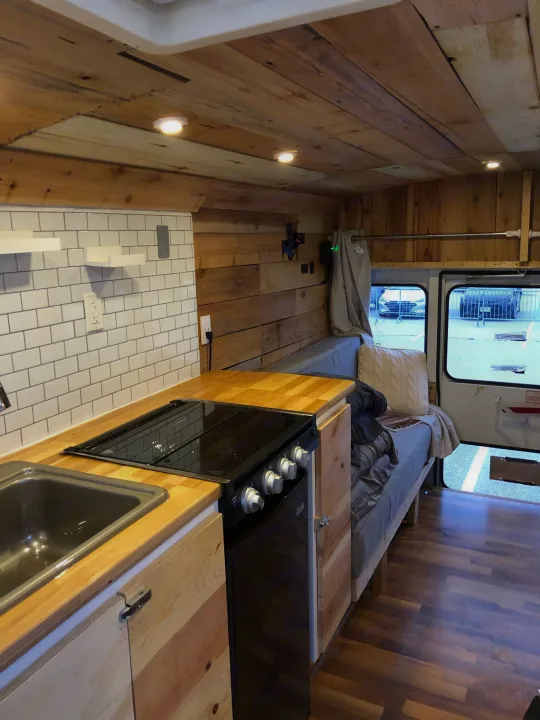 RV rental: Cozy wood-paneled van conversion interior with kitchen, bed, subway tile backsplash, and warm lighting.. Chevy Express 3500 Mini Bus 2002