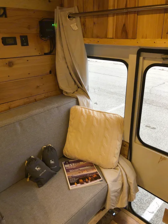 Inside a comfy RV rental: wood-paneled walls, a cozy bench, pillow, and solar power setup for off-grid adventures.. Chevy Express 3500 Mini Bus 2002