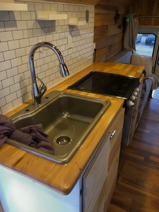 RV rental kitchen area: modern sink, stovetop, wood counters, and white subway tile backsplash, offering a cozy travel setup.. Chevy Express 3500 Mini Bus 2002