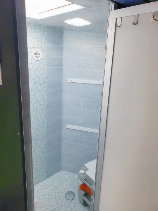 Inside an RV rental: a bright, compact bathroom with a shower, portable toilet, and handy shelving.. Neo Trailer NAV105S 2020
