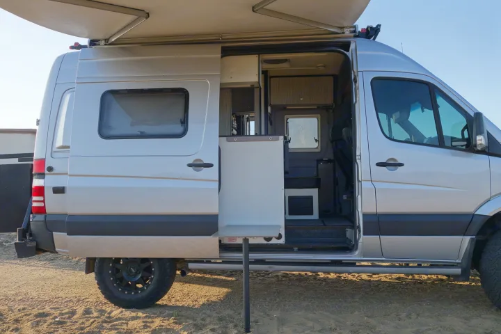 Silver camper van with open side door, extended awning, and table setup, ready for an RV rental trip or van life adventure.. Winnebago Revel 2019