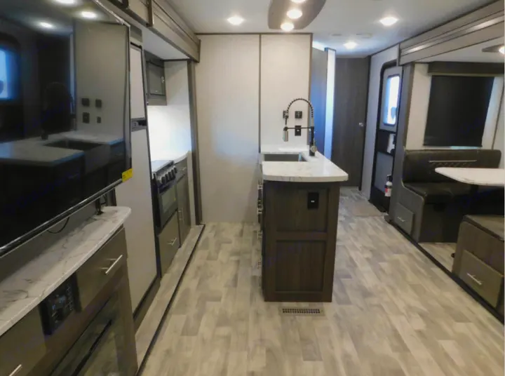 Explore this bright rv rental interior featuring a full kitchen, dining booth, living area with TV, and light wood flooring.. Dutchmen Other 2021