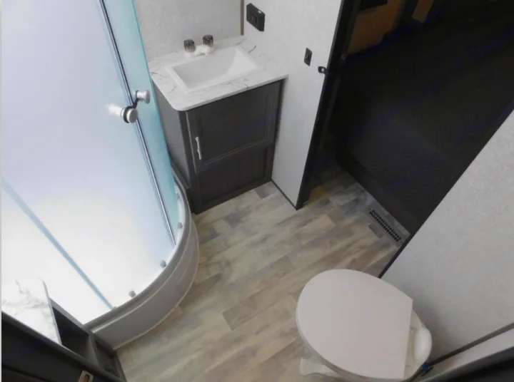 This RV rental bathroom features a frosted curved shower, vanity, toilet, and light wood-look flooring, connecting to a bedroom.. Dutchmen Other 2021