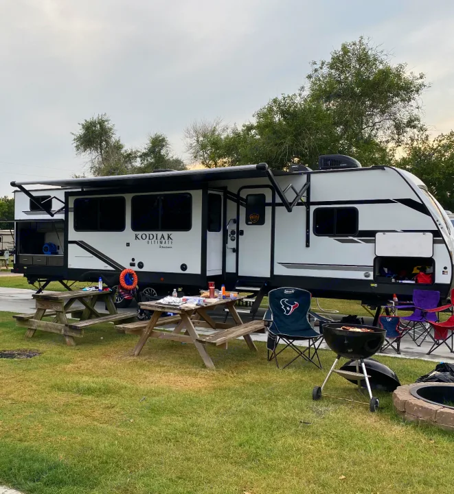 Enjoy this comfortable RV rental setup at a scenic campsite, featuring picnic tables, a grill, and fire pit for outdoor leisure.. Dutchmen Other 2021