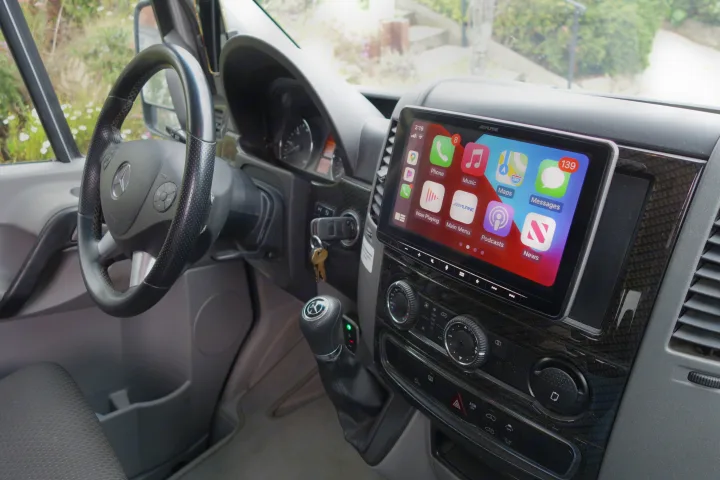 Inside an RV rental Mercedes-Benz Sprinter van: an upgraded Alpine Apple CarPlay screen, steering wheel, and controls are shown.. Winnebago Revel 2019
