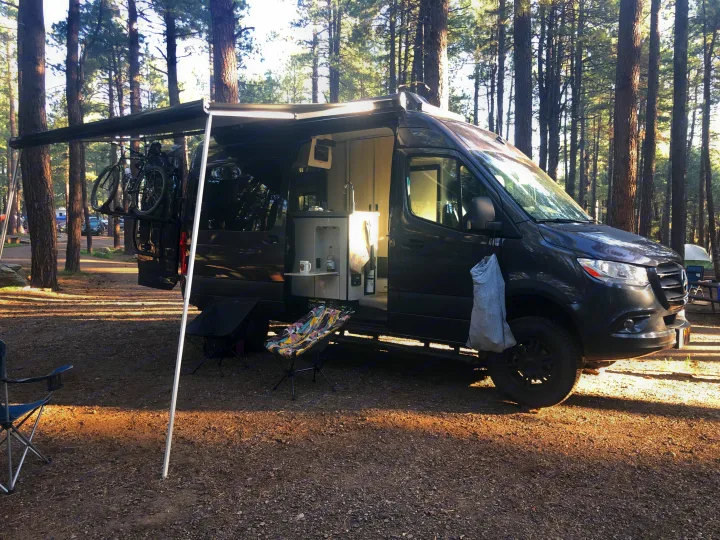 Explore the forest with this RV rental: a Sprinter camper van, complete with an awning, bike rack, & open kitchen area for camping.. Mercedes-Benz 4x4 Sprinter mwb 2021