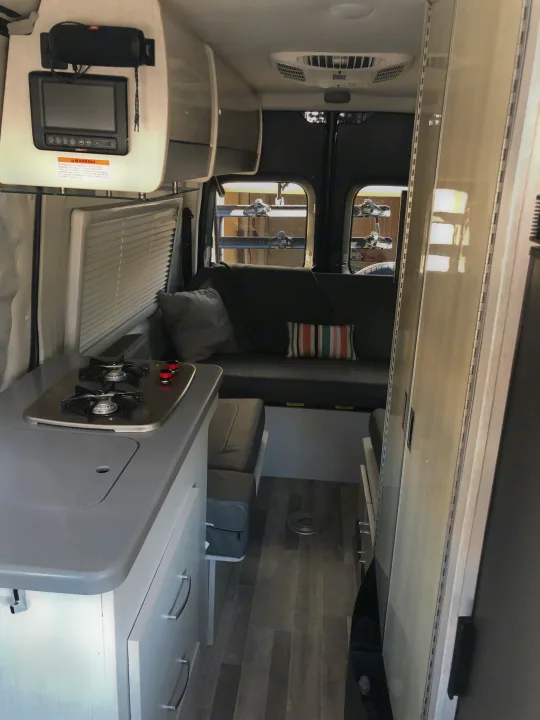 Step inside this inviting RV rental interior: compact kitchen, cozy sofa lounge, and integrated tech. Perfect for your next trip.. Mercedes-Benz 4x4 Sprinter mwb 2021