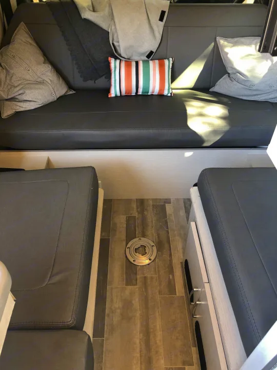 Cozy RV rental interior with comfortable grey seating, patterned pillows, and a table base on wood-look flooring.. Mercedes-Benz 4x4 Sprinter mwb 2021
