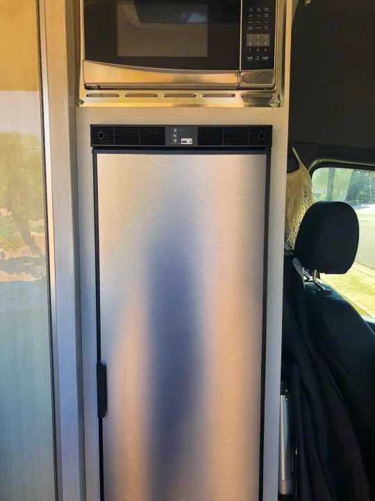 Inside an RV rental: a built-in stainless steel microwave over a Norcold refrigerator, perfect for mobile cooking.. Mercedes-Benz 4x4 Sprinter mwb 2021