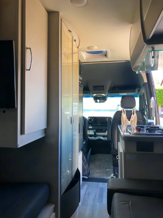 View inside an RV rental: This camper van features a kitchen with stove/sink, seating, and the driver's cab beyond.. Mercedes-Benz 4x4 Sprinter mwb 2021