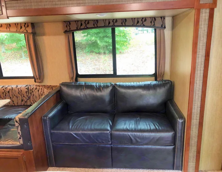 Cozy RV rental interior featuring a black leather sofa with white stitching, large windows, and a dinette.. Keystone Passport 2017