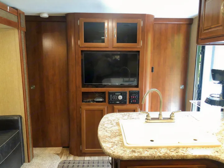 An RV rental's well-equipped interior: a built-in entertainment system, kitchen sink, and warm wood tones.. Keystone Passport 2017
