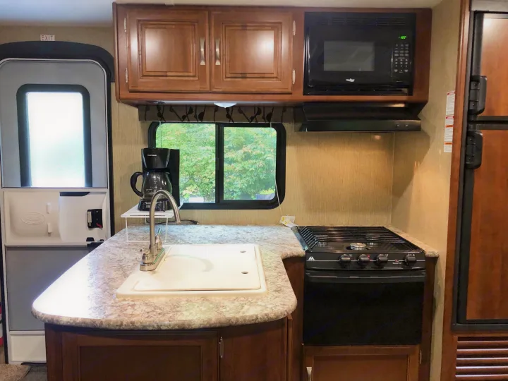 Well-equipped RV rental kitchen: sink, stove, microwave, fridge, and cabinets. Ready for your travels and camping trips.. Keystone Passport 2017