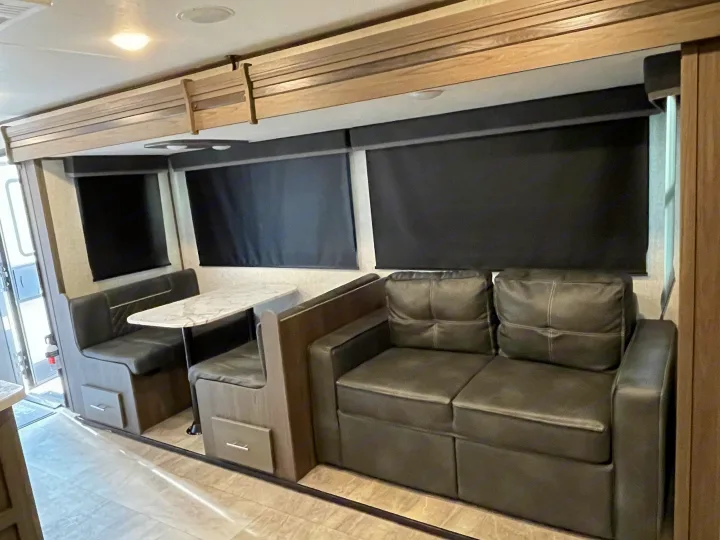 RV rental interior with a dark gray dinette, marble-look table, and a plush sofa. Blackout blinds are visible.. Dutchmen Other 2021