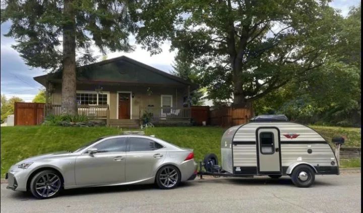 A Lexus sedan tows a compact Little Guy teardrop RV rental on a residential street. Ready for a cozy road trip adventure.. Riverside RV Retro 2017
