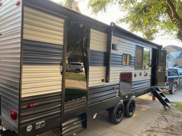 A sleek gray and black travel trailer, likely an RV rental, parked outside with its entry door open and steps extended.. Forest River Cherokee Grey Wolf 2021