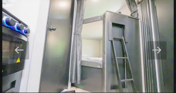 RV rental interior featuring a compact kitchen (left) with illuminated knobs, plus bunk beds with ladder & curtain.. Forest River Cherokee Grey Wolf 2021