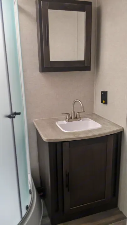 This compact RV rental bathroom features a small white sink, dark wood cabinets, and a framed mirror, offering essential amenities.. Crossroads Cruiser Aire 2022