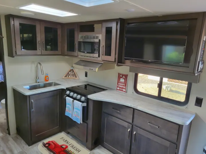 RV rental interior: compact kitchen with sink, stove, microwave, cabinets, and TV. Ideal for camping trips.. Grand Design 265bh 2021