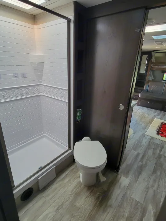 Inside an RV rental, this bright bathroom features a white shower and toilet, with a sliding door leading to the main living space.. Grand Design 265bh 2021