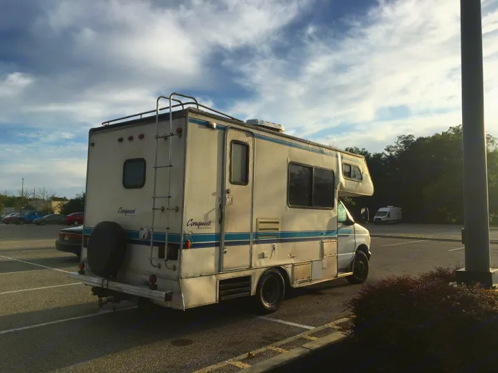 Conquest Class C RV rental parked in a lot, viewed from the rear-side, with a ladder and spare tire.. Gulf Stream Conquest 1998
