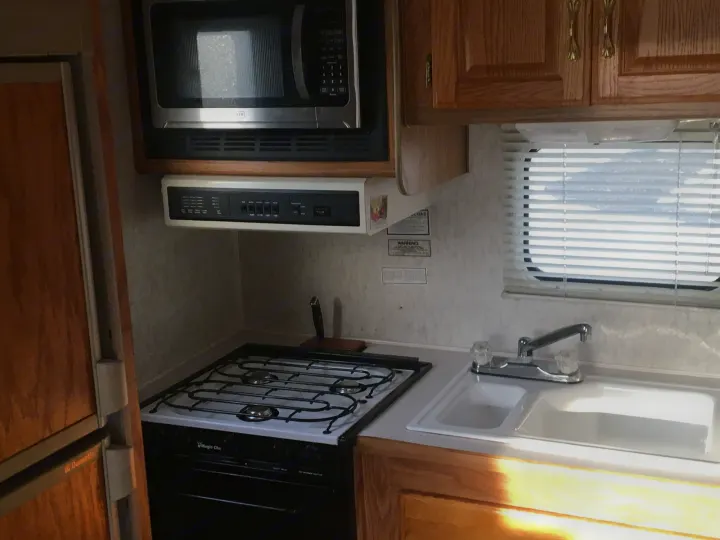 Inside an RV rental: Compact kitchen featuring a microwave, gas stove/oven, double sink, and Dometic fridge.. Gulf Stream Conquest 1998
