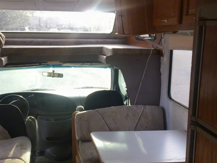 RV rental interior: driver's view, over-cab bunk, and dinette with table & seating. Bright light from front window.. Gulf Stream Conquest 1998