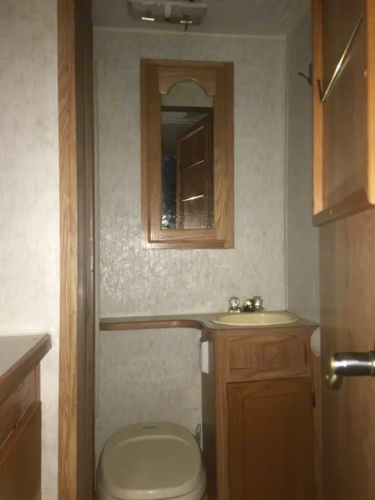 RV rental: Compact bathroom with a toilet, small vanity, sink, mirror, and warm wood cabinetry.. Gulf Stream Conquest 1998