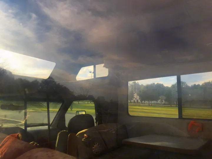 Relaxing inside an RV rental with reflections on windows, viewing a scenic park and bright sky.. Gulf Stream Conquest 1998