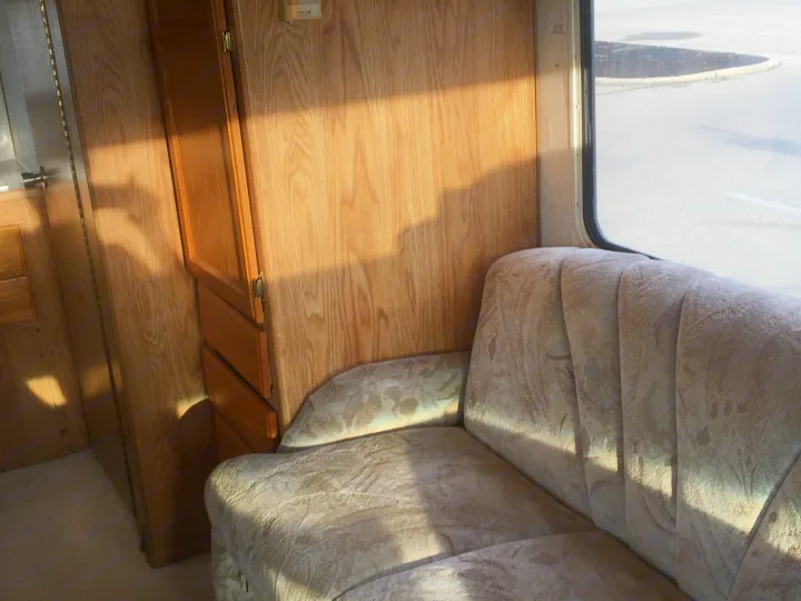 Inside a sunny RV rental: oak wood walls, a plush sofa, and a parking lot view from the window, illuminated by natural light.. Gulf Stream Conquest 1998