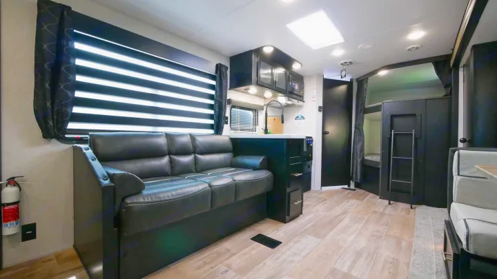 Modern RV rental interior featuring a black sofa living area, compact kitchen, and bunk beds with a ladder.. Forest River Cherokee Grey Wolf 2021