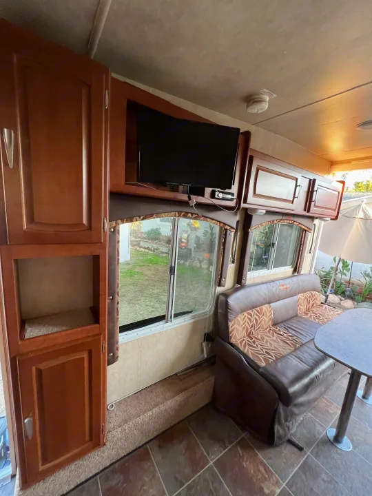 Cozy RV rental interior featuring a comfortable dinette with patterned cushions, a mounted TV, and wood cabinetry.. Forest River Stealth 2012