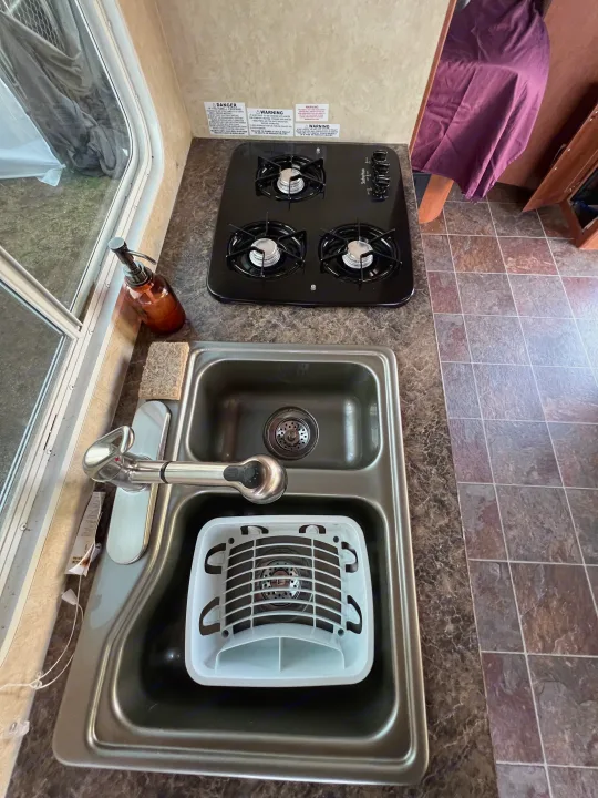 RV rental: The kitchen area, complete with a 3-burner stove, double sink, and warning labels, designed for compact living.. Forest River Stealth 2012