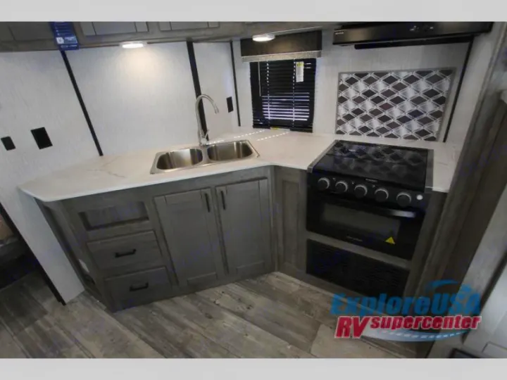 This clean RV rental kitchen features a double sink, gas stove, and modern cabinetry, ideal for travels.. Heartland North Trail 2021