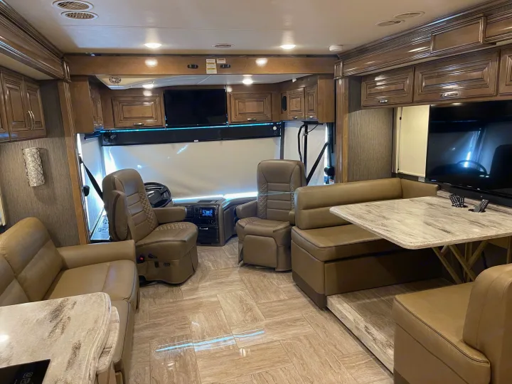 Spacious, luxurious RV rental interior featuring light wood cabinets, tiled floor, and comfortable seating with modern amenities.. Thor Motor Coach Aurora 2020