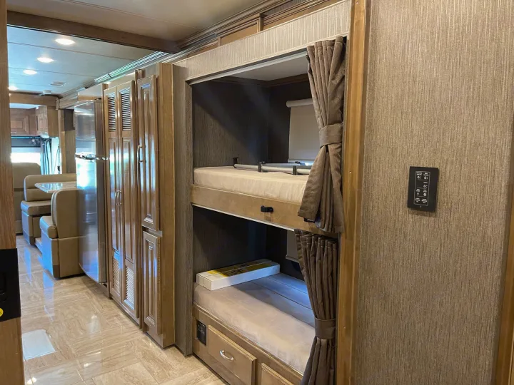 Modern RV rental interior showcasing comfy bunk beds with privacy curtains, a full kitchen, and dinette area.. Thor Motor Coach Aurora 2020