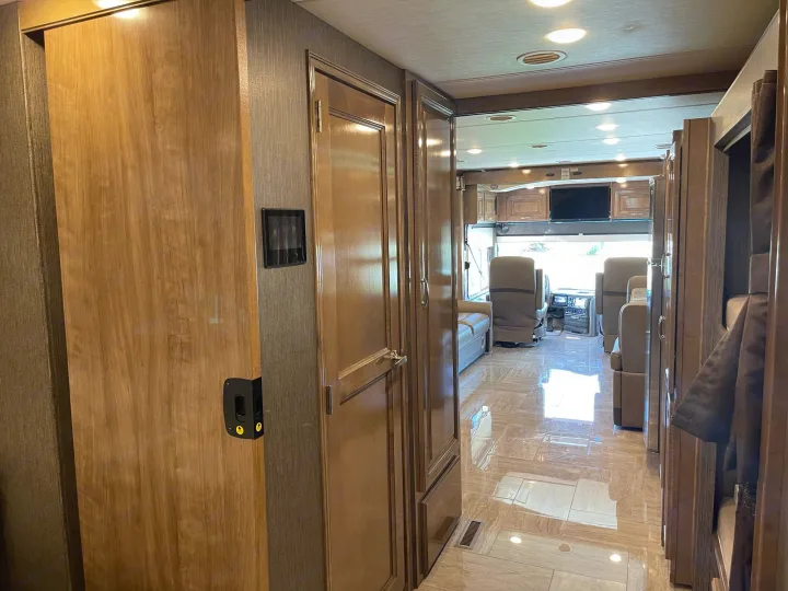 Inside an RV rental: a spacious hallway with warm wood accents, gleaming tile floor, leading to the front living area.. Thor Motor Coach Aurora 2020