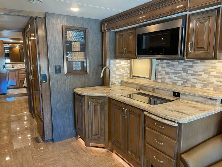 Explore a luxury RV rental's modern kitchen: built-in microwave, induction cooktop, sink, and wood cabinetry.. Thor Motor Coach Aurora 2020