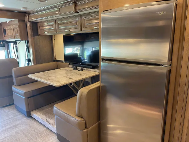 RV rental interior: cozy dinette booth with table, overhead cabinets, flat-screen TV, and stainless steel Whirlpool refrigerator.. Thor Motor Coach Aurora 2020