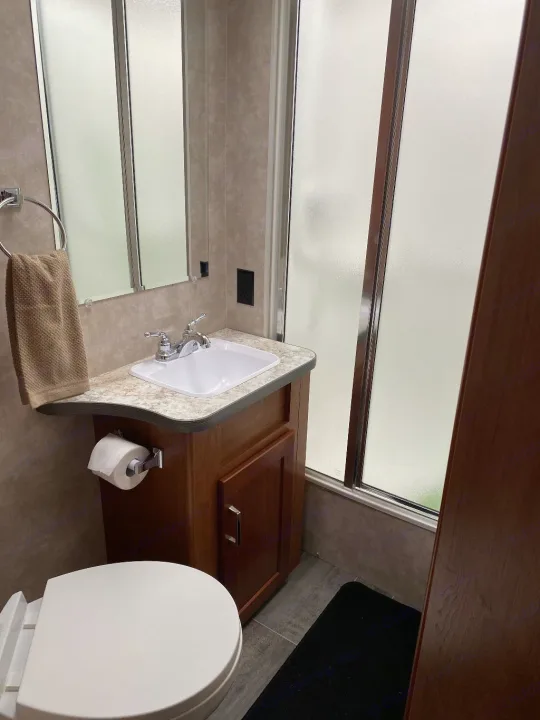 Compact bathroom in an RV rental, featuring a sink, toilet, and shower with frosted glass.. Winnebago Minnie Winnie 2019